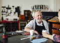 Senior craftsman sitting at table with young craftswoman and smiling in book arts workshop